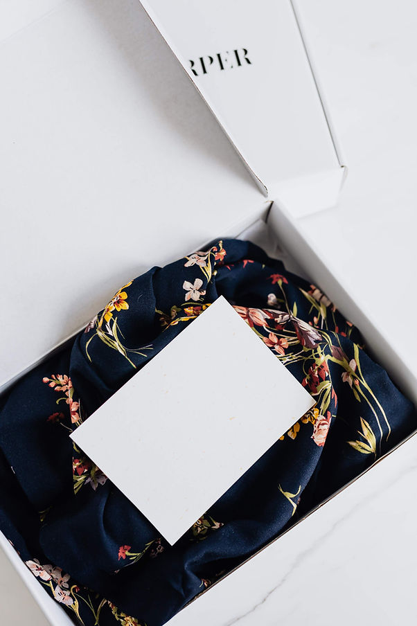 White branded shipping box with chrome company logo in middle of box. Foreground box is open with floral clothing inside and a white note.