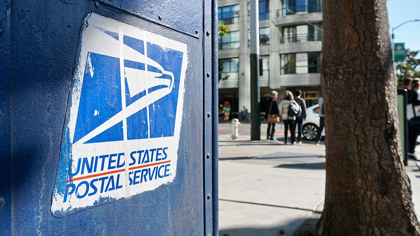Worn down USPS sticker on side of mailbox at the side of a busy street. 